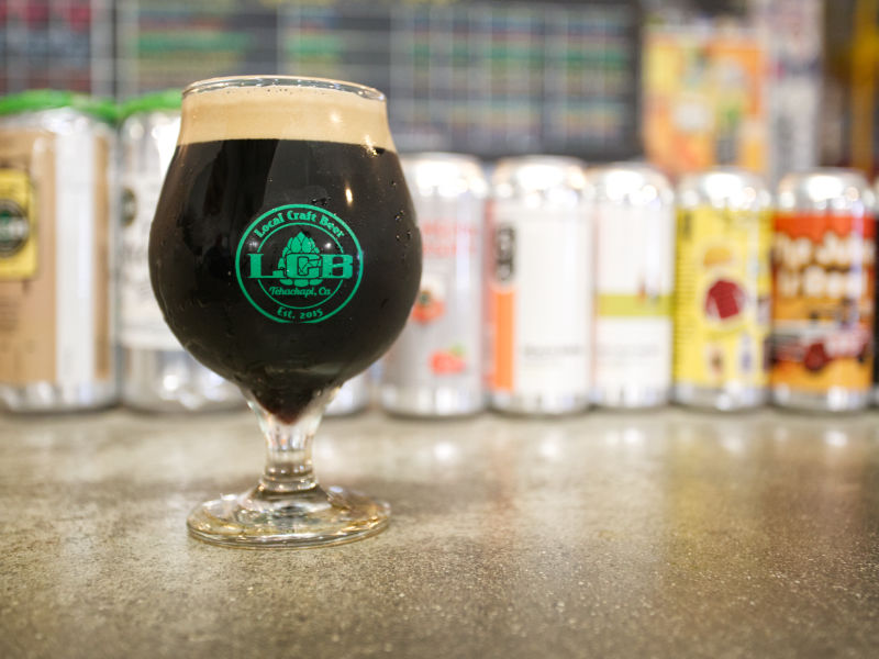 Glass of cold dark beer sitting on counter in front of line up of beer cans.